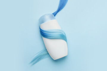 Bottle of shampoo and hair strand on color background