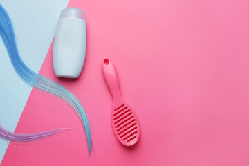 Bottle of shampoo, brush and hair strands on color background