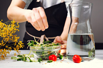 A woman prepares a salad of green sprouts with tomatoes, seeds and drinking water. Healthy Detox Food