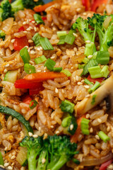 Asian rice with vegetables: zucchini, broccoli, red bel pepper, mushrooms, carrot, spring onion and sesame seeds. Dish isolated in a blue bowl, close-up on a black marble background. Asian cuisine.