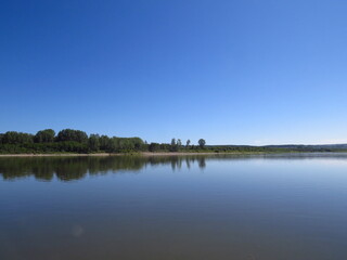 Quiet surface of the river. Beautiful cloudless warm summer day. Trees on the island in the background