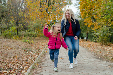 A little girl walks and plays with her mother in the park. Autumn landscape with golden leaves