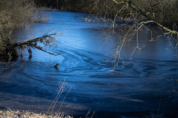 A beautiful picture of a small pond covered with ice. Blue icy water with trees in the background