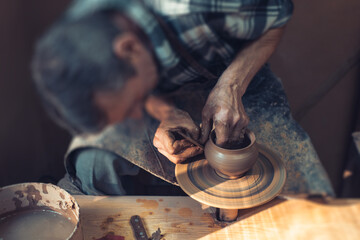 A male artisan in a pottery workshop makes a piece of clay behind a pottery wheel. Traditional pottery craft.