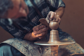 A male artisan in a pottery workshop makes a piece of clay behind a pottery wheel. Traditional pottery craft.