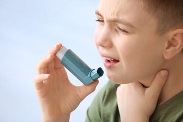 Little boy with inhaler having asthma attack on light background