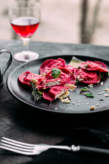 Beetroot ravioli with cheese in a black plate on the table near the window