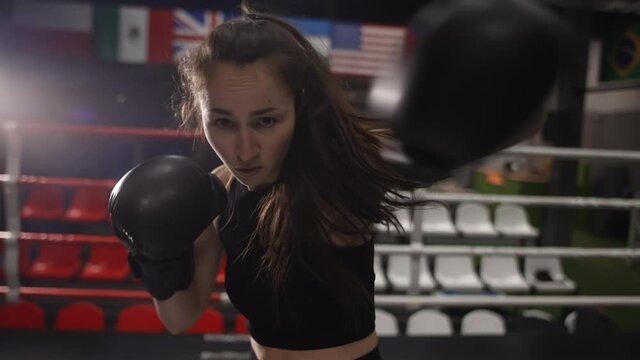Female boxer punching camera, shadow boxing during workout in dark gym