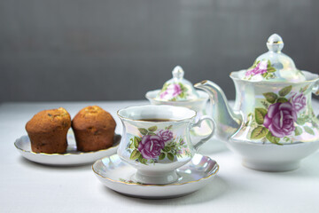 A cup of tea on a white tablecloth. Tea with muffins. Light breakfast. White tea set with flowers.