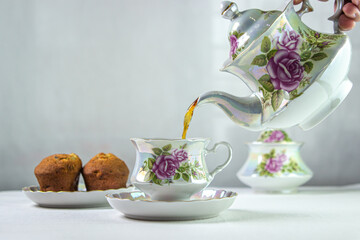 Tea is poured into a cup. A cup of tea on a white tablecloth. Light breakfast. White tea set with flowers.