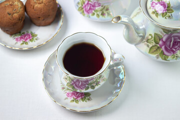 A cup of tea on a white tablecloth. Tea with muffins. Light breakfast. White tea set with flowers.