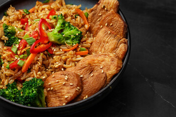 Asian rice with teriyaki chicken and vegetables: zucchini, broccoli, red pepper, mushrooms, carrot, spring onion. Dish isolated in a blue bowl, close-up on a black marble background. Asian cuisine.