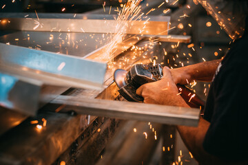 an adult man is seen working cutting a piece of metal in an industrial workshop, sparks are seen
