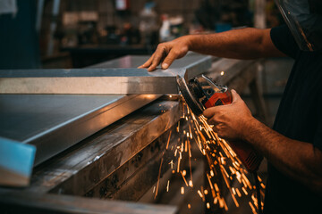 an adult man is seen working cutting a piece of metal in an industrial workshop, sparks are seen