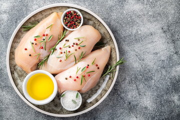 Raw uncooked chicken breasts with spices and herbs on gray concrete table, chicken meat with ingredients for cooking. Top view.