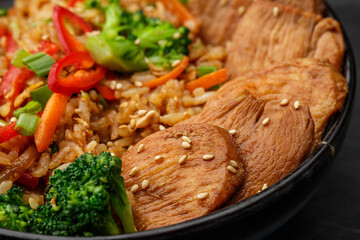 Asian rice with teriyaki chicken and vegetables: zucchini, broccoli, red pepper, mushrooms, carrot, spring onion. Dish isolated in a blue bowl, close-up on a black marble background. Asian cuisine.