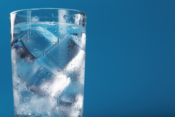 A glass with ice water and ice cubes on a blue background.