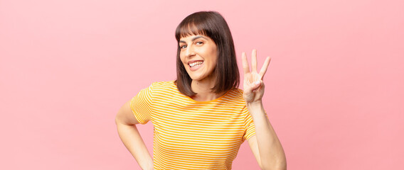 pretty woman smiling and looking friendly, showing number three or third with hand forward,...