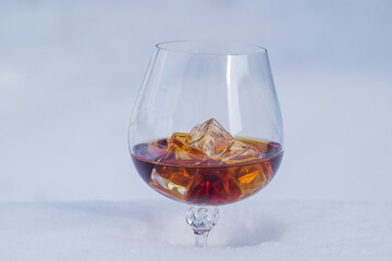 Glass of cognac with ice on a bed of snow and white background, close up