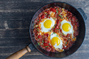 Shakshuka, fried eggs with tomatoes, onion, red pepper and spices in cast iron pan
