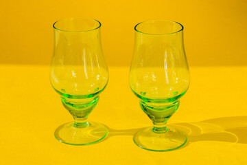 two empty green goblets of glass stand on a yellow background. Horizontal photo, close-up.