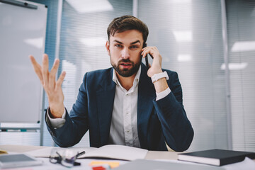 Frustrated adult entrepreneur listening to colleague during phone conversation