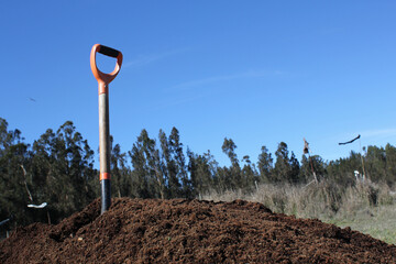 shovel over a pile of brown soil ready for planting, in the rural field