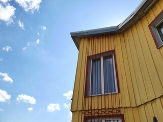 A building with yellow walls against a clear sky. Small windows look out onto the street, offering a view of the clear sun.