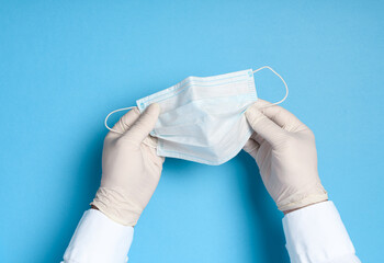 hands in medical gloves with a medical breathing mask on a blue background, health care prevention...