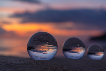 Three clear crystal balls of three sizes are sphere reveals  seascape view with spherical .placed on the sand at Karon Beach during sunset.