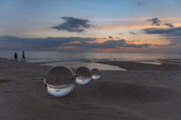 Three clear crystal balls of three sizes are sphere reveals  seascape view with spherical .placed on the sand at Karon Beach during sunset.
