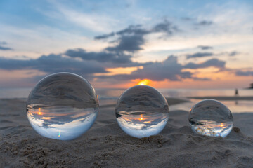 Fototapeta na wymiar Three clear crystal balls of three sizes are sphere reveals seascape view with spherical .placed on the sand at Karon Beach during sunset.