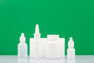 Medication bottles with eye drops, nasal spray, pills and ear drops on white table against green background with copy space. Concept of health care and medication