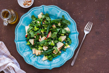 Healthy salad with kale, apple and almonds in a blue plate on a brown concrete background. Kale recipes.