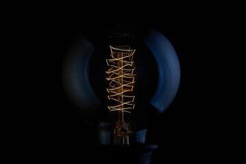 Electric vintage Edison light bulb with a spiral on a blue background. Retro style lamp