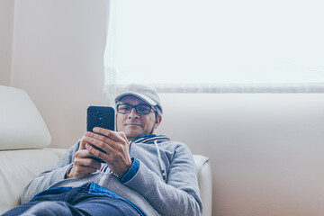 middle aged man is using a smart phone and smiling while sitting on sofa at home