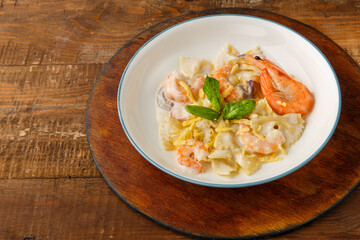 Pasta with shrimps in a creamy sauce on a gray plate on a wooden table on a stand.