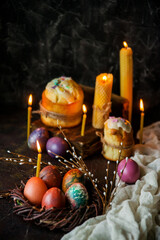 easter cake, candles, willow branches and painted eggs as a symbol of Easter on a dark background, wooden table