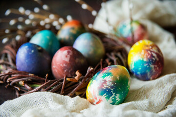 Colorful Easter eggs in a decorative nest, next to willow branches on a dark background, a copy of the space