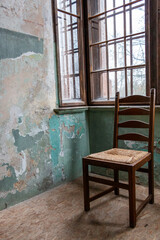 Old wooden chair in abandoned room with wooden windows.