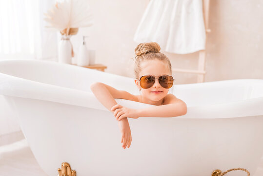 Baby girl sitting in the bathroom. Portrait of a cute girl in sunglasses in a bright bathroom.