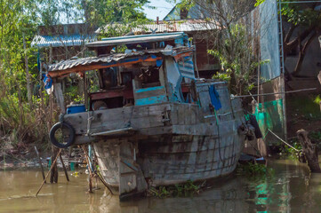 Fototapeta na wymiar altes, zerfallendes Fischerboot liegt am Ufer des Mekong. Im Hintergrund, Häuser aus Wellblech