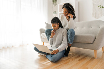 Mother and daughter sitting on sofa at home with laptop