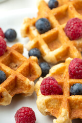 Top view of waffles with raspberries and blueberries, selective focus, on white plate, in vertical