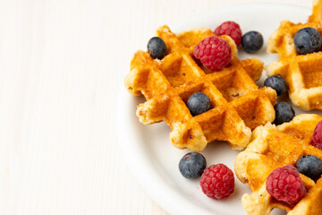 Aerial view of waffles with raspberries and blueberries, on plate, selective focus, on white table, horizontal, with copy space
