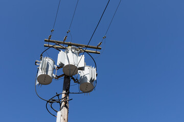 Fototapeta premium Tall wood electric pole with three transformers against a clear, deep blue sky, horizontal aspect