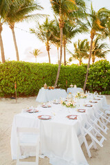 Outdoor dining table for small party on beach with palm trees in the background
