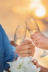 bride and groom closeup of hands holding champagne glasses with sea and sunset in background