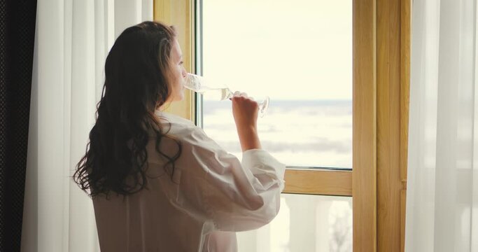 4K Video of dreamy lone female drinking champagne looking at window in loneliness. Single lonely romantic woman