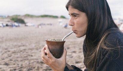 Young woman drinking traditional Argentinian yerba mate at the beach.